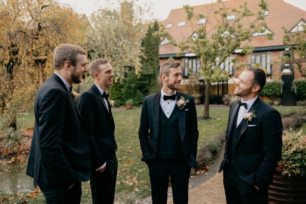 Groom and groomsmen stand in garden smiling