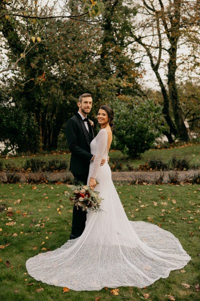 Grooms hands around brides waist as they stand on leaves and green grass