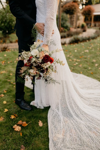 Bride and groom stand on the grass she holds bouquet they hug