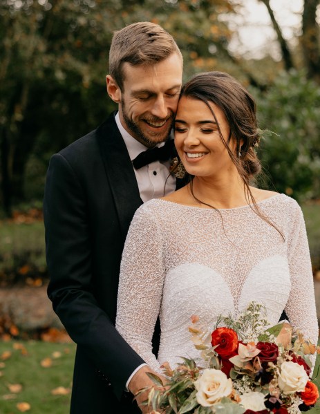 Groom hugging bride from behind as she smiles exterior grass garden shot