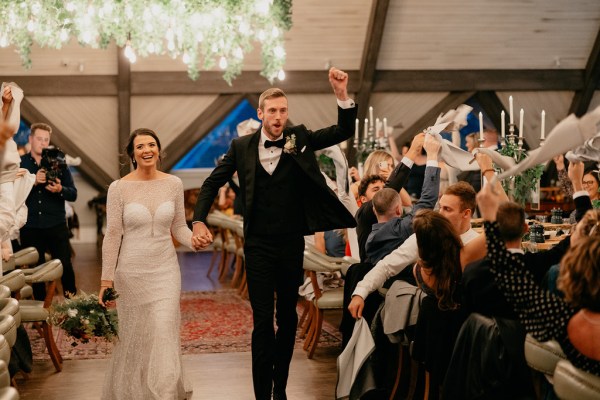 Bride and groom walk passed guests seated in dining room/ballroom they celebrate smile