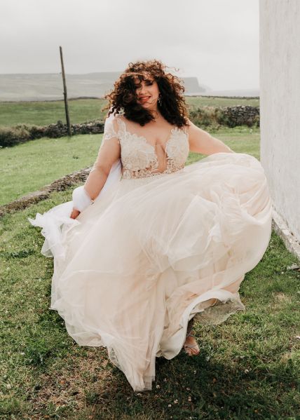 Bride shows off her long dress dancing on grass