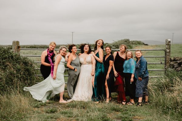 Bride bridesmaids stand in front of gate gated farm setting grass