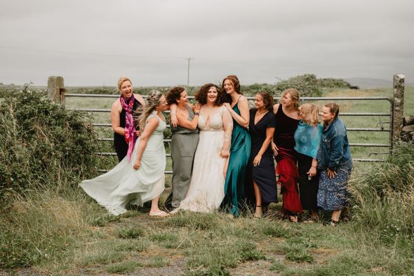 Bride bridesmaids stand in front of gate gated farm setting grass