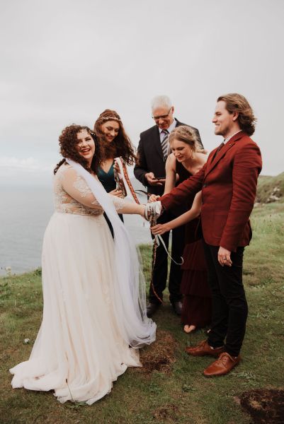 Bride and groom tie ribbon around hands with celebrant cliff setting two witnesses bridesmaids