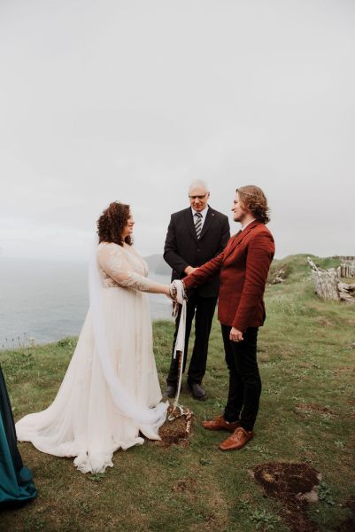 Bride and groom tie ribbon around hands with celebrant cliff setting