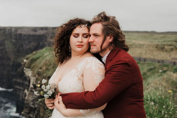 Bride and groom hug embrace on grass cliff edge Irish landscape