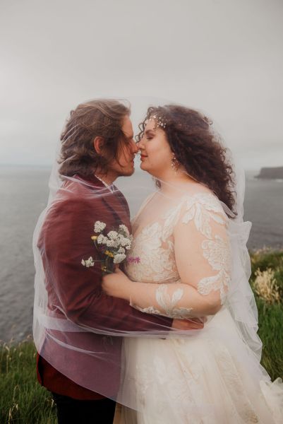 Bride and groom stand on grass setting sea cliff wind is blowing close up