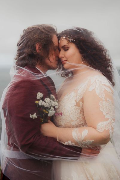 Bride and groom stand on grass setting sea cliff wind is blowing close up