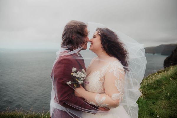 Bride and groom stand on grass setting sea cliff wind is blowing close up