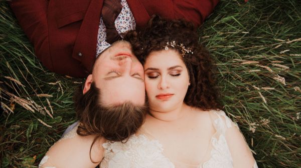 Bride and groom lie on the grass together with eyes closed smiling