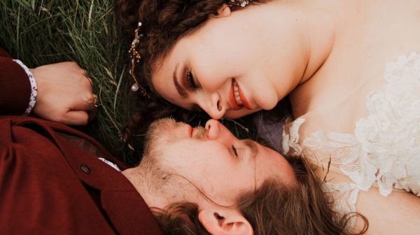 Bride and groom lie on the grass together facing each other