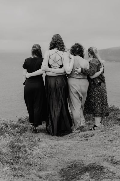 Bridesmaids stand on top/edge of cliff windy landscape setting sea in background black and white