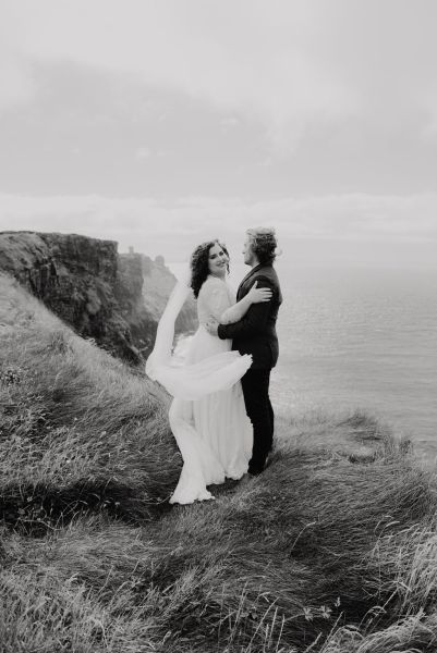 Bride and groom veil in the air Clare setting sea on the top of a cliff Irish landscape black and white