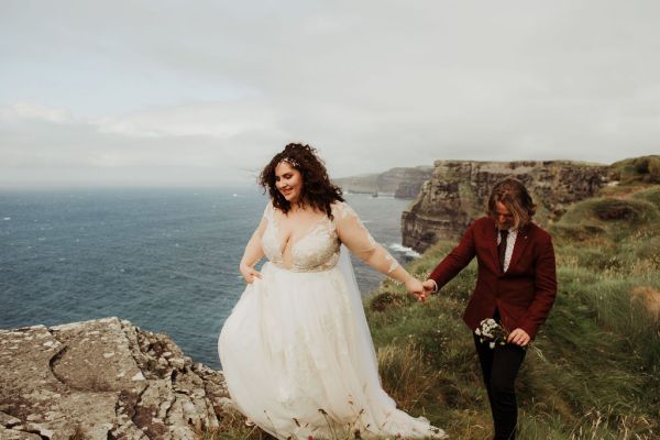 Bride and groom holding hands cliff setting in background and sea