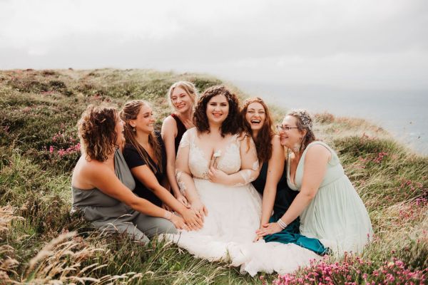 Bride bridesmaids sitting on edge of cliff Irish setting landscape laughing smiling