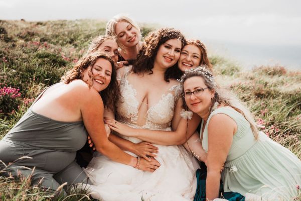 Bride bridesmaids sitting on edge of cliff Irish setting landscape laughing smiling