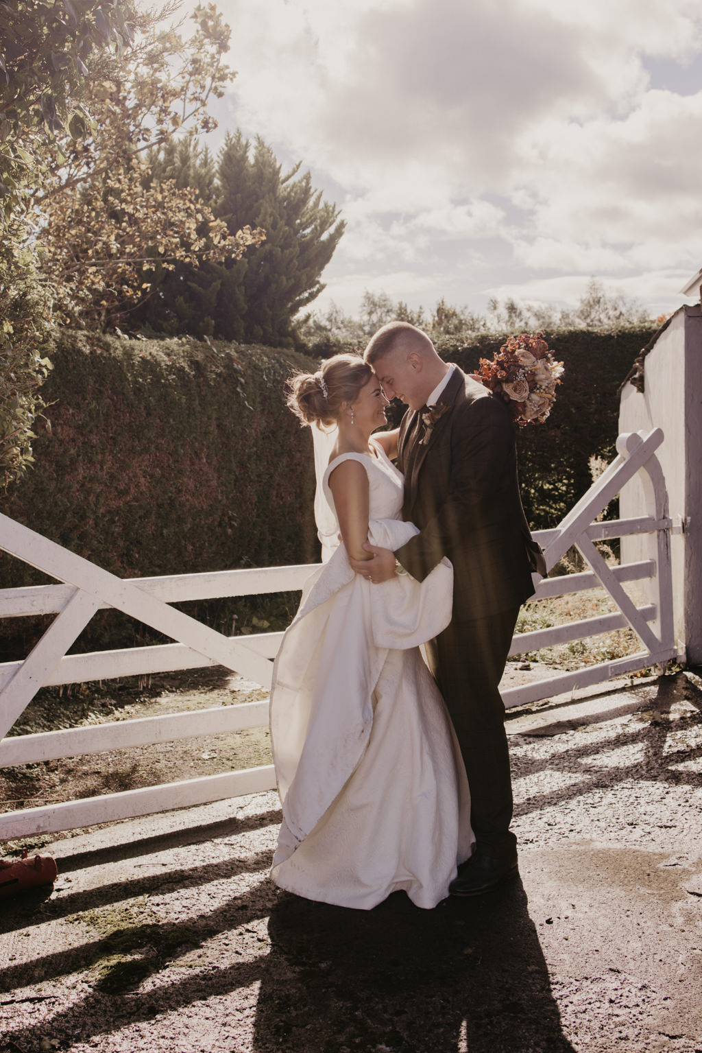 Bride and groom touch foreheads in front of white gate