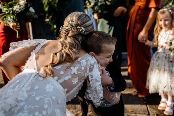 Bride hugs little boy in black tuxedo suit