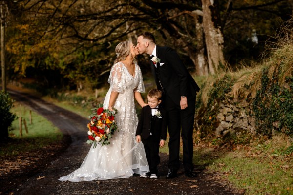 Bride and groom kiss son in between them pathway forest park setting