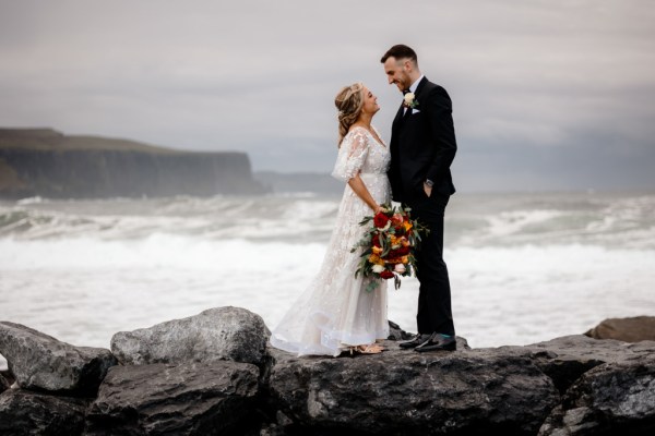 Bride and groom in front of sea setting Kerry mountains on clifftop looking at each other