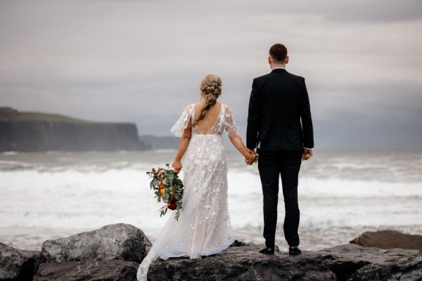 Bride and groom in front of sea setting Kerry mountains on clifftop looking at each other