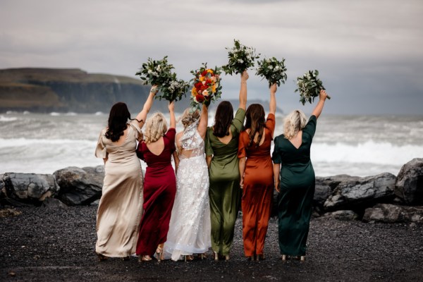 Bride and bridesmaids on their own in front of scenic sea Kerry mountains and clifftop bouquet and flowers in hand in the air from behind