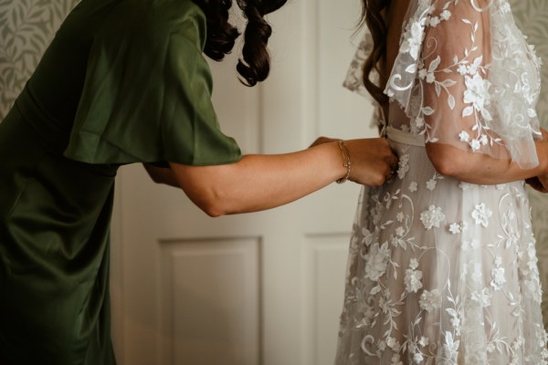 Bridesmaid helps bride with back of dress zip button getting ready close up