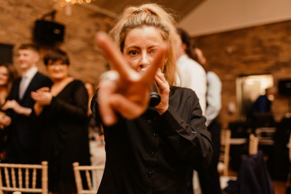 Woman holds up fingers peace sign into camera