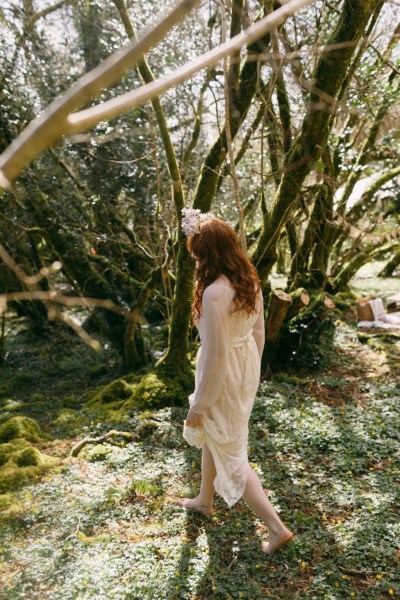 Arms either side of model bride as she wears floral flower headband dances in forest setting walking away