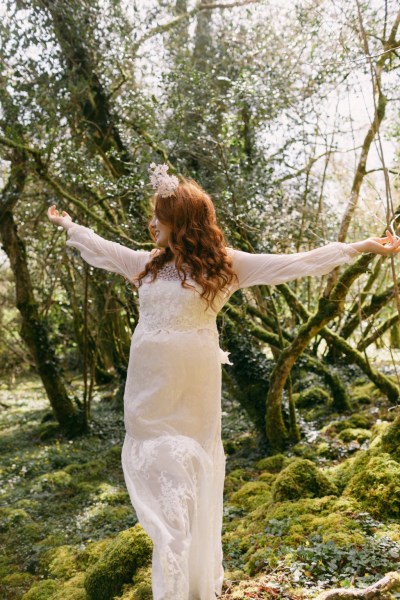 Arms either side of model bride as she wears floral flower headband dances in forest setting