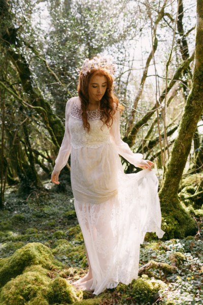 Arms either side of model bride as she wears floral flower headband dances in forest setting shows off white dress