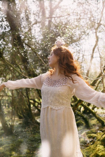 Arms either side of model bride as she wears floral flower headband dances in forest setting