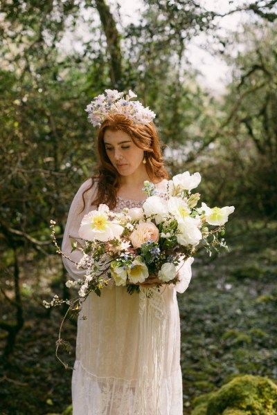 Model bride wearing elaborate floral flower headband holding bouquet in forest