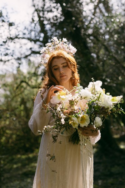 Model bride wearing elaborate floral flower headband holding bouquet in forest