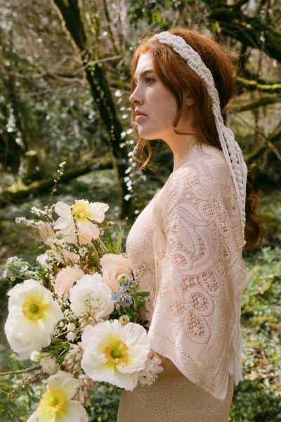 Model bride wearing headband walking around in forest from behind string ribbon detail holding bouquet of flowers hair detail red head