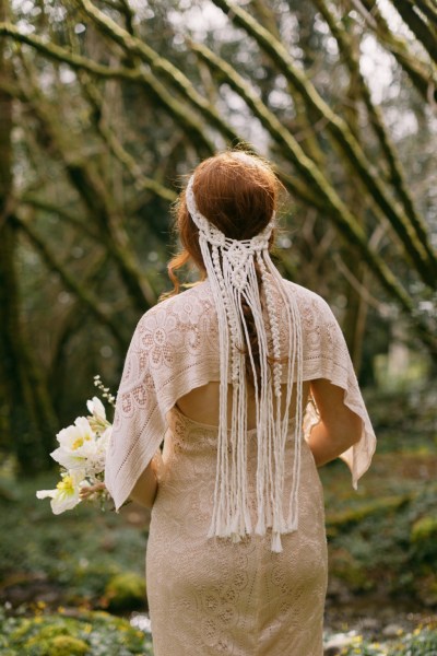 Model bride wearing headband walking around in forest from behind string ribbon detail holding bouquet of flowers