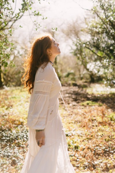 Model bride looks up sun shining down on her in forest