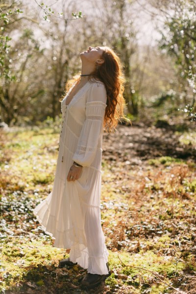 Model bride looks up sun shining down on her in forest