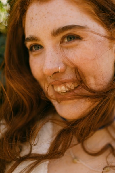 Hair blowing in the wind covering model brides face as she smiles and laughs