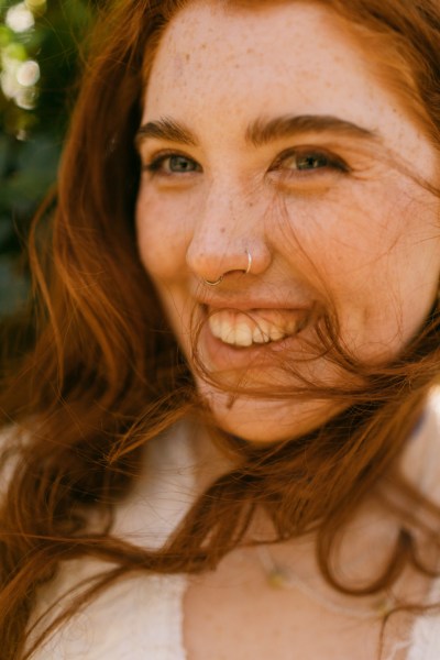 Hair blowing in the wind covering model brides face as she smiles and laughs