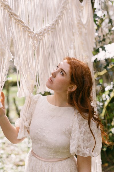 Close up of red headed bride woman model earrings looking at string ribbon decor in forest