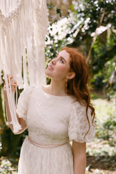 Close up of red headed bride woman model earrings looking at string ribbon decor in forest