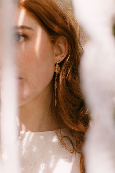 Model bride through string decor exterior forest setting red hair and earring detail