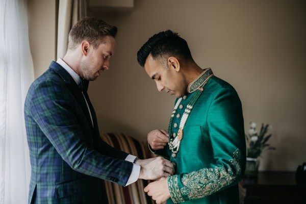 Grooms help each other get ready at window bowtie