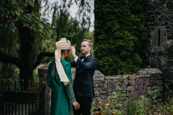 Grooms in garden placing hat on head