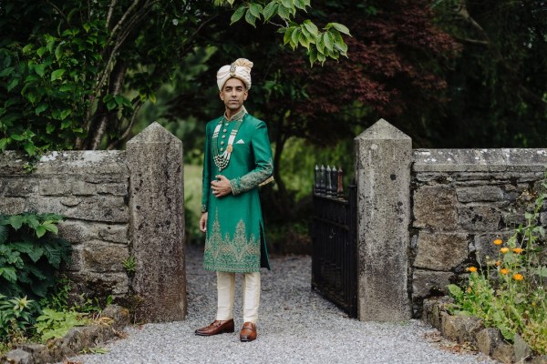 Groom stands in front of black gate to garden