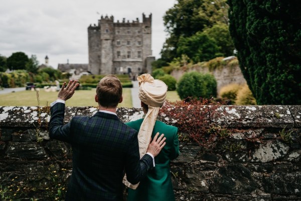 Grooms wave and look at venue castle in distance