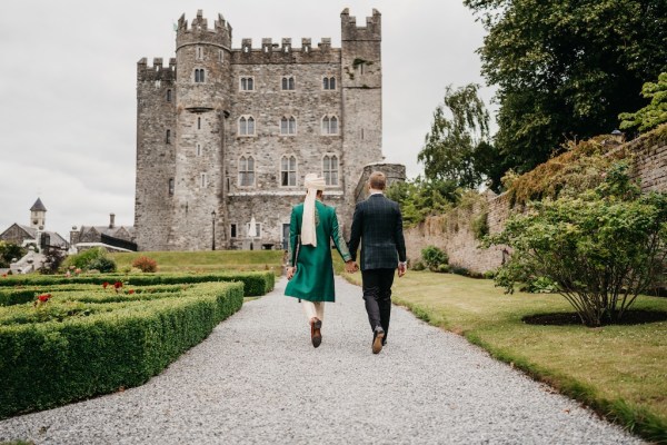 Grooms hand in hand holding hands walking towards castle