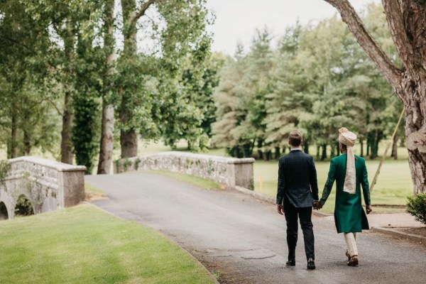 Grooms hand in hand walking towards bridge in hotel